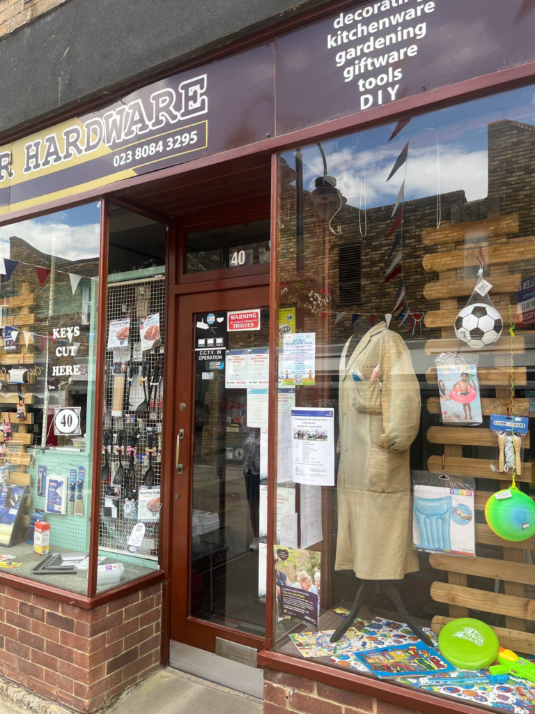 R Hardware shop window display in Hythe, featuring tools, gardening supplies, and gifts.