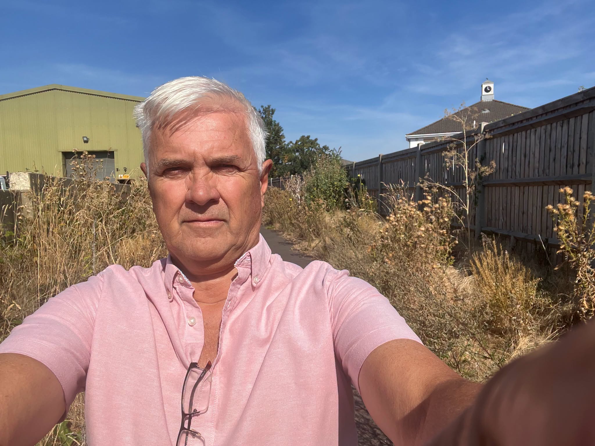 Man in pink shirt walks down overgrown path near industrial building