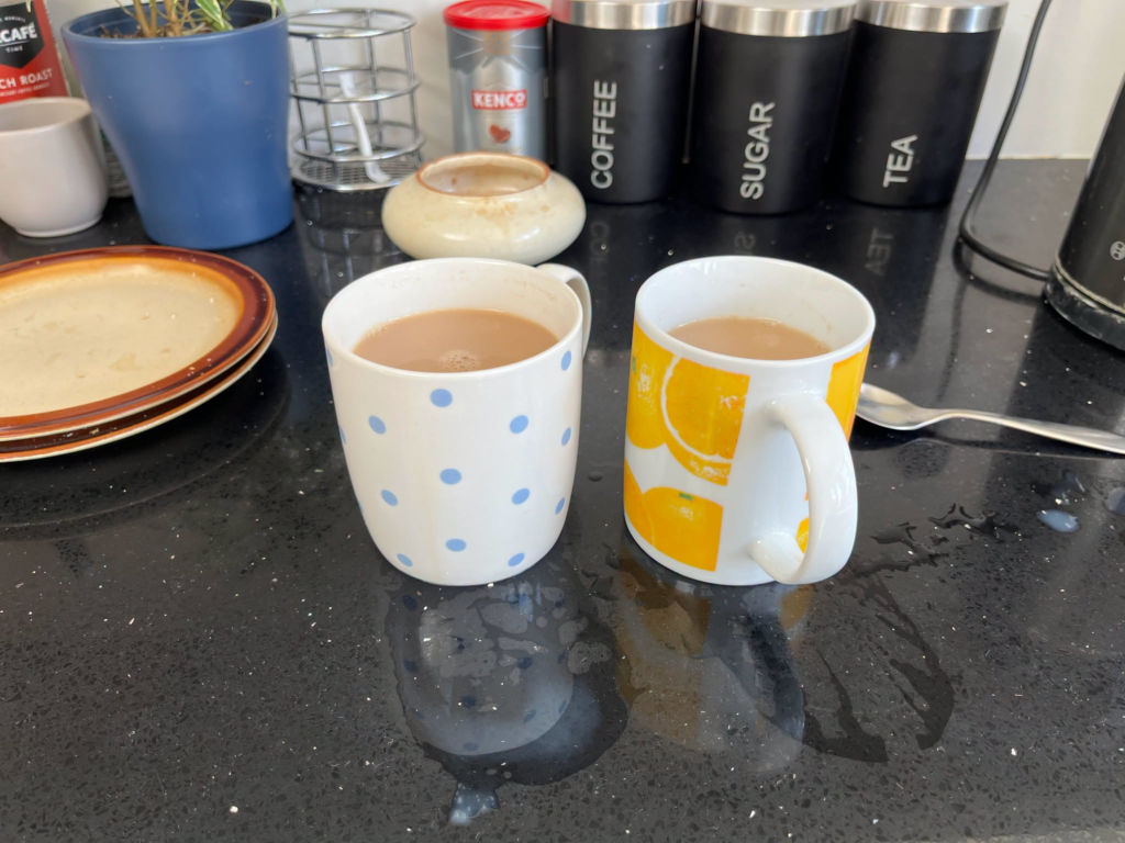Two mugs of tea on a kitchen counter, one blue with white polka dots, one yellow with oranges.