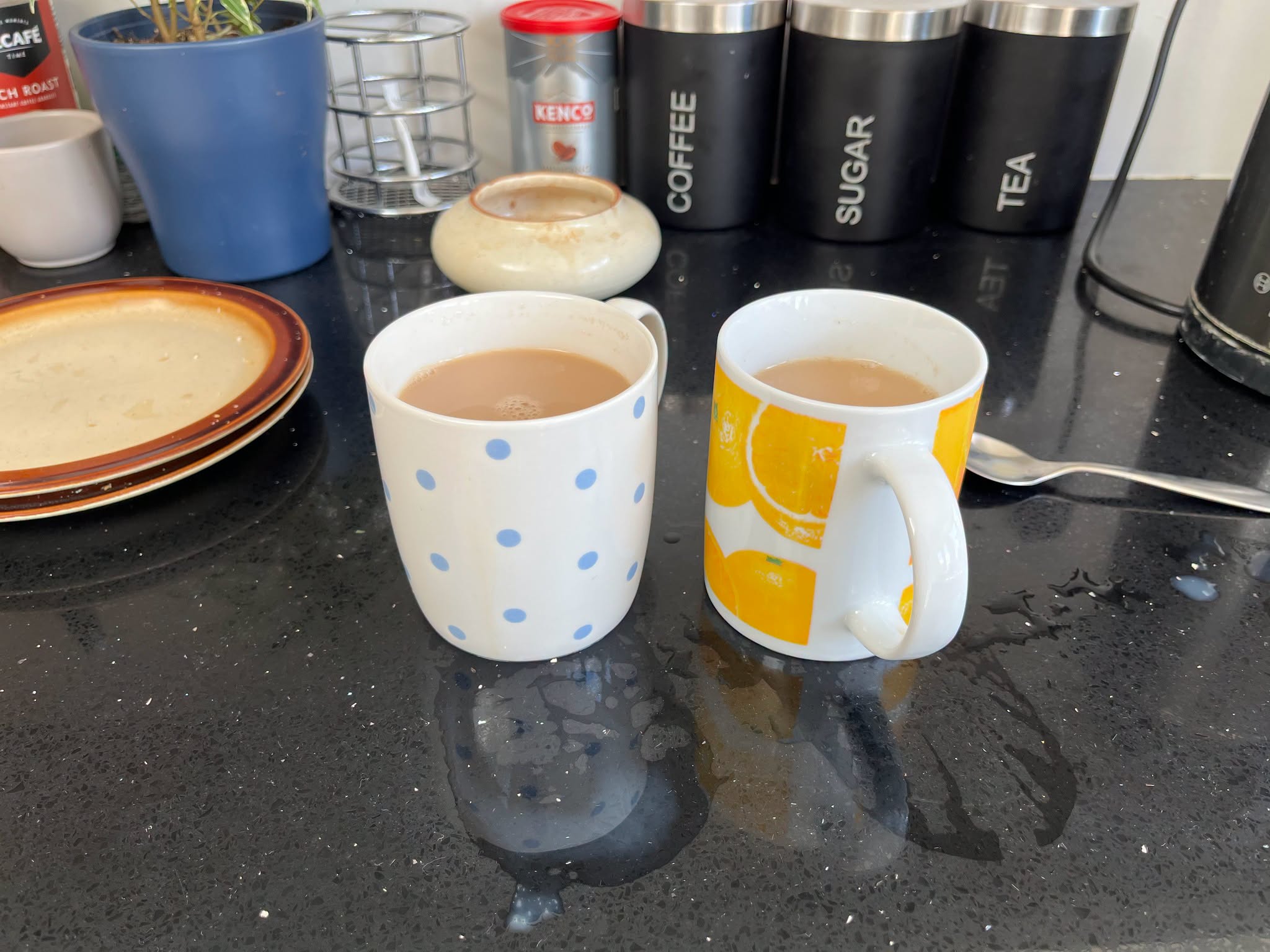 Two mugs of tea on a kitchen counter, one blue with white polka dots, one yellow with oranges.