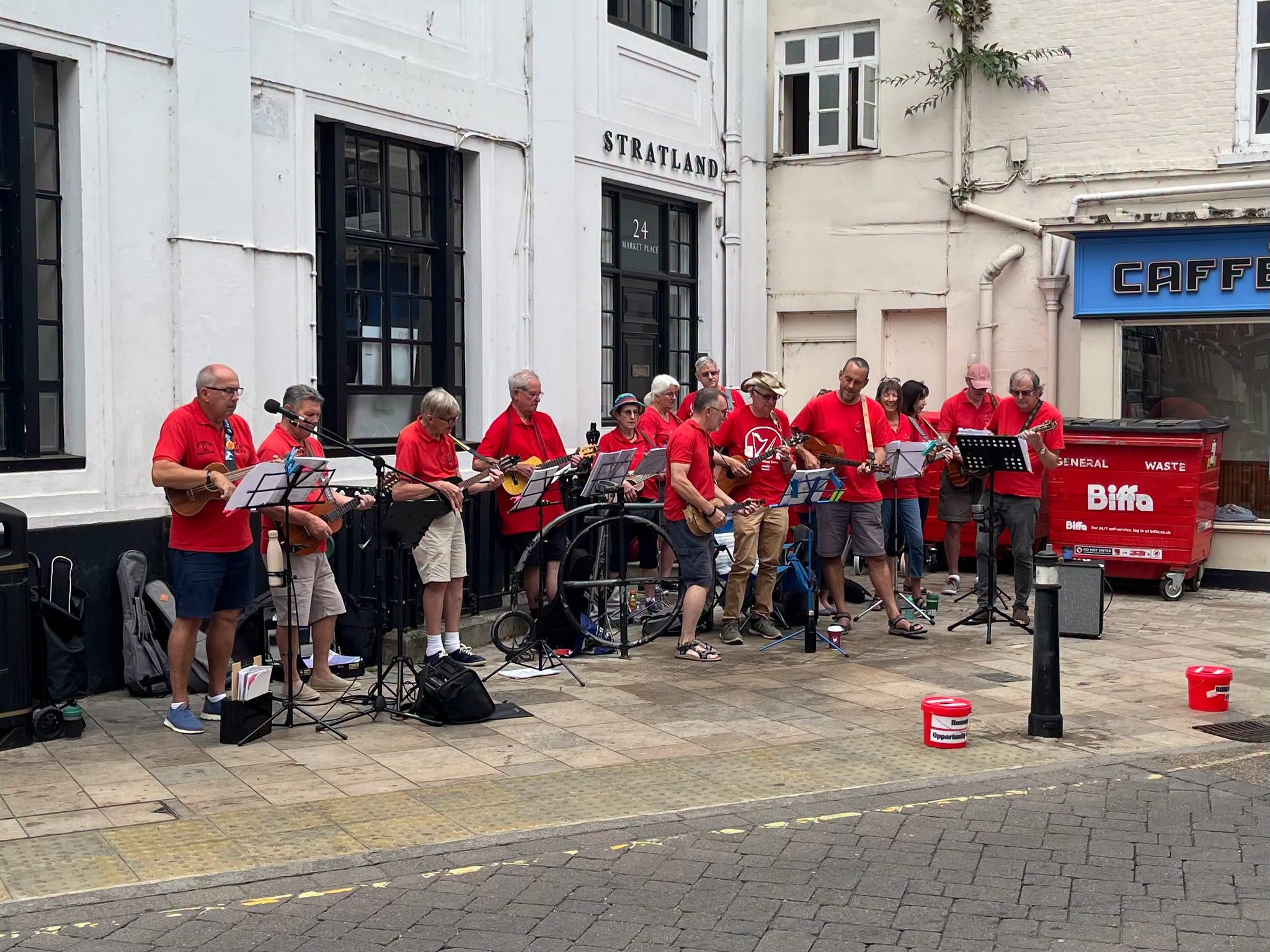 Ukulele band plays music on a street in front of a building with a cafe
