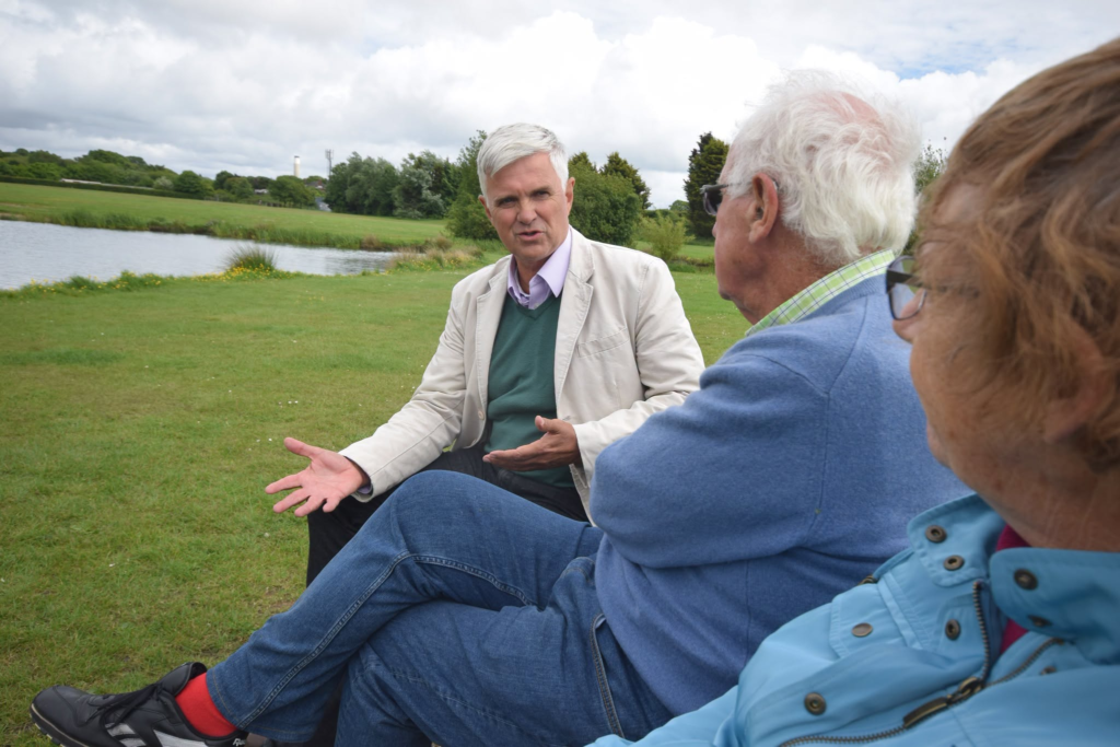 Three people in casual outdoor discussion near a lake