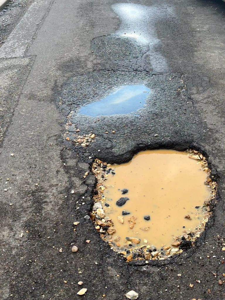 Large, deep pothole filled with muddy water on a cracked asphalt road.