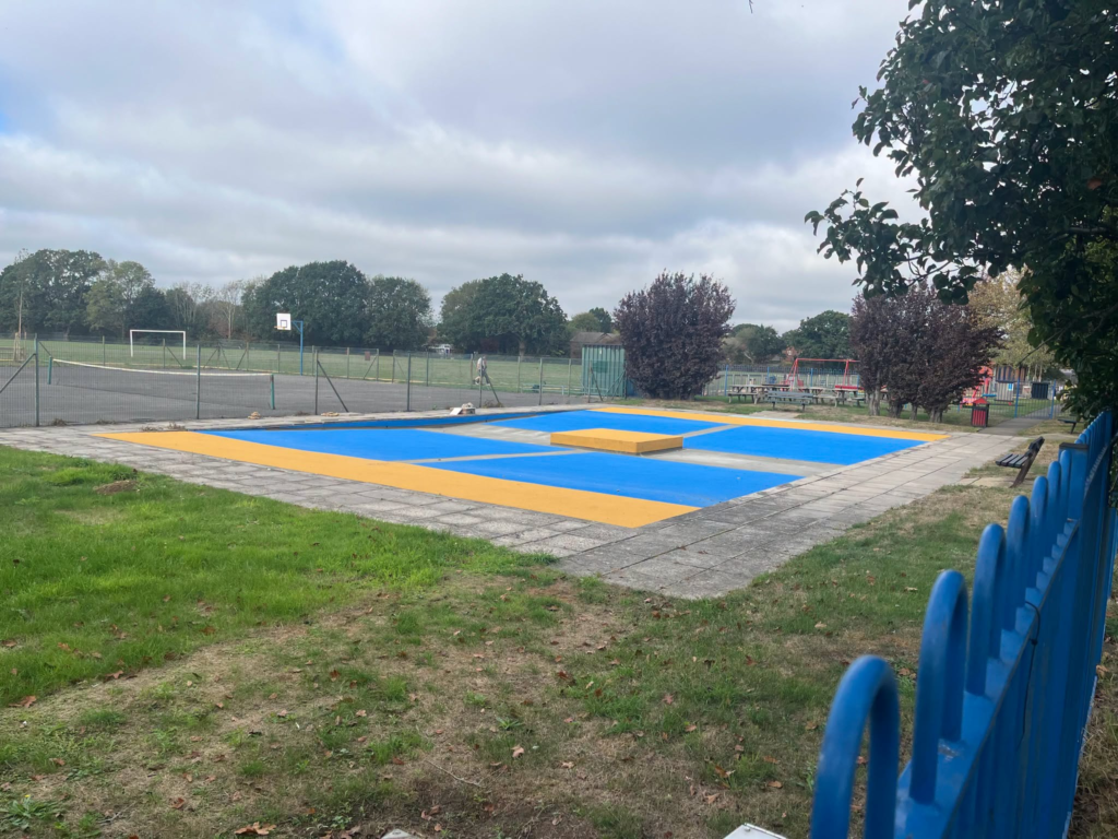 Testwood splash pad with blue and yellow surfacing in grassy park.