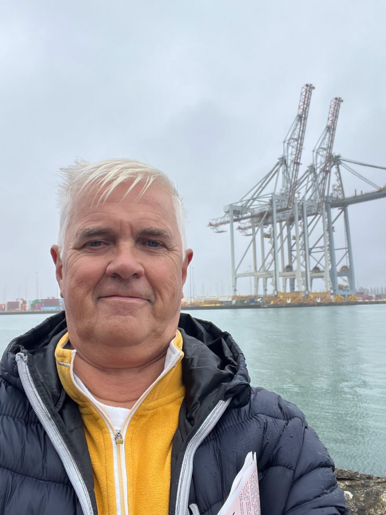 Man in front of large port cranes and water