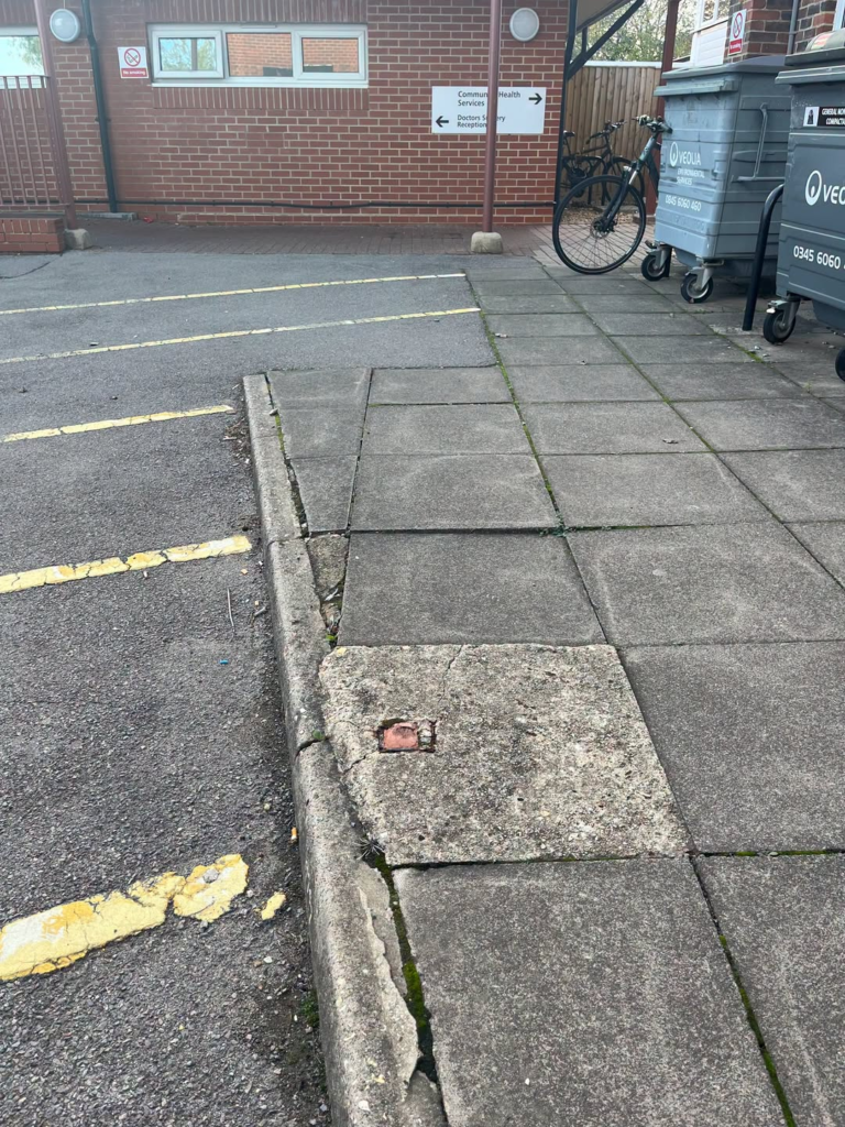 Uneven paving slabs and a cracked curb create a tripping hazard.