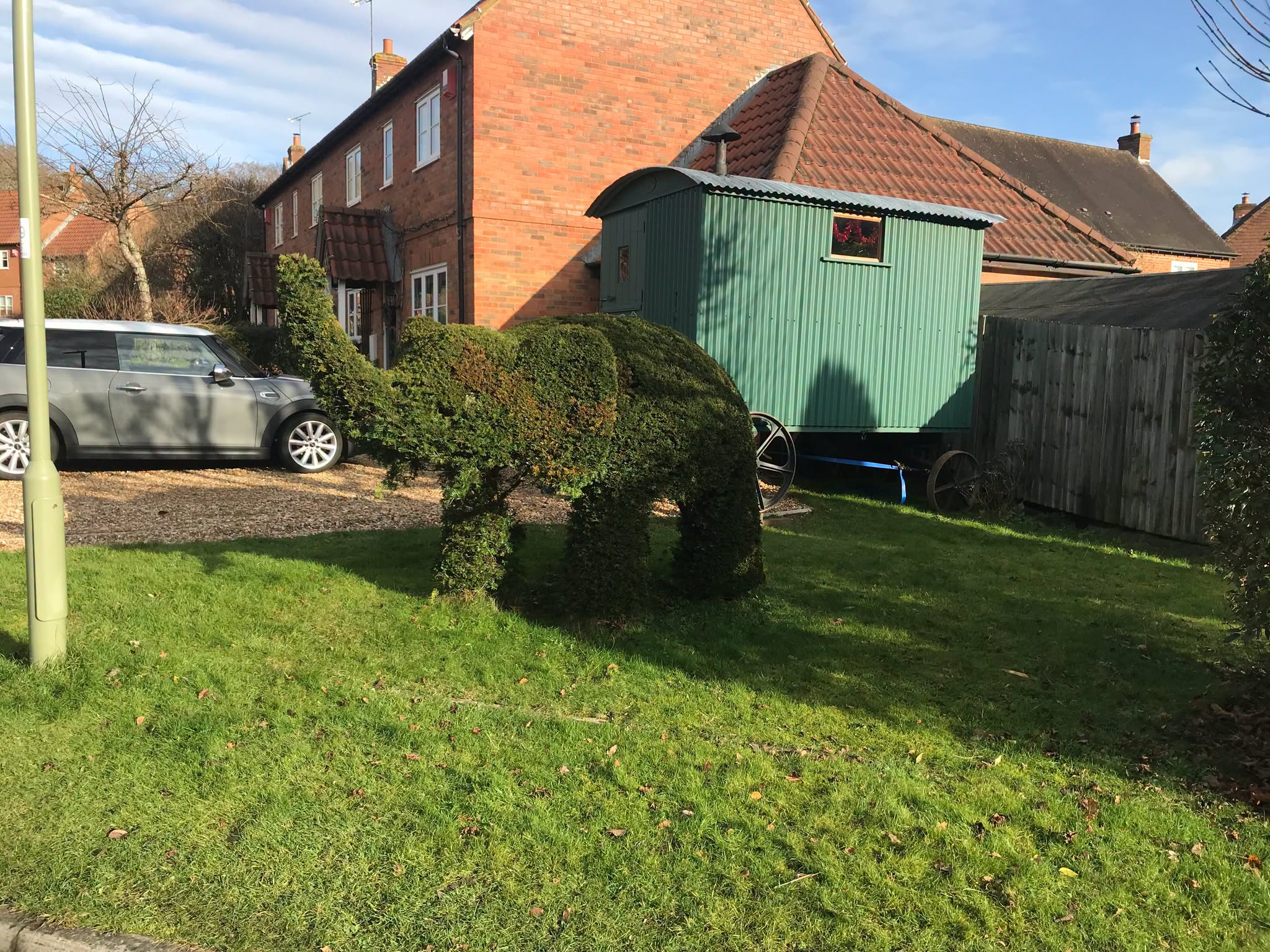 Elephant-shaped topiary on a lawn, with a green shepherd's hut and car in the background.