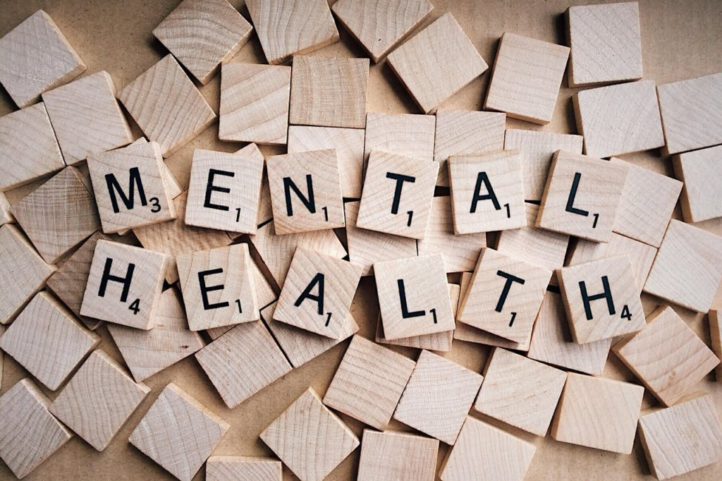 Wooden Scrabble tiles spell out "MENTAL HEALTH" on a bed of loose tiles.