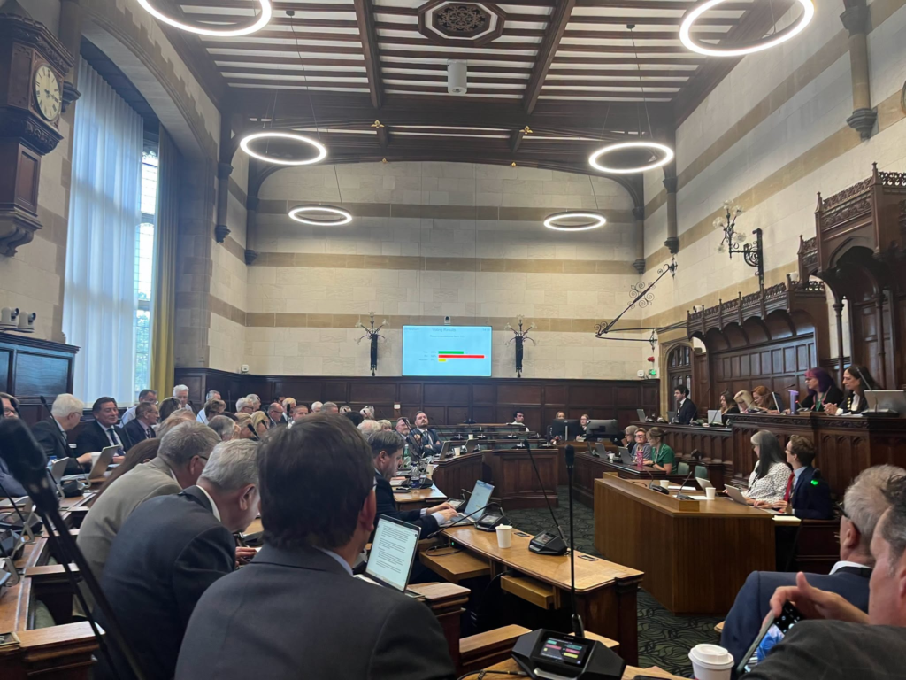 Parliamentary debate in session with audience and screen displaying data